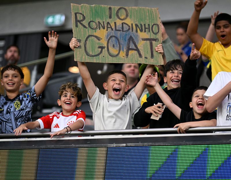 Young soccer fans show their enthusiasm at a sports event, celebrating a legendary athlete with signs and cheers.